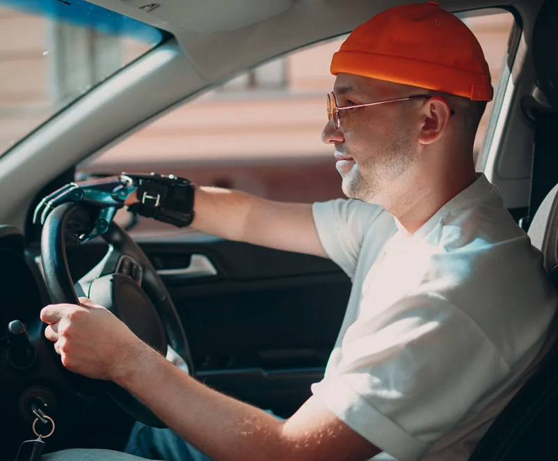 male with a prosthetic arm, red beanie hat and white shirt driving a car   
